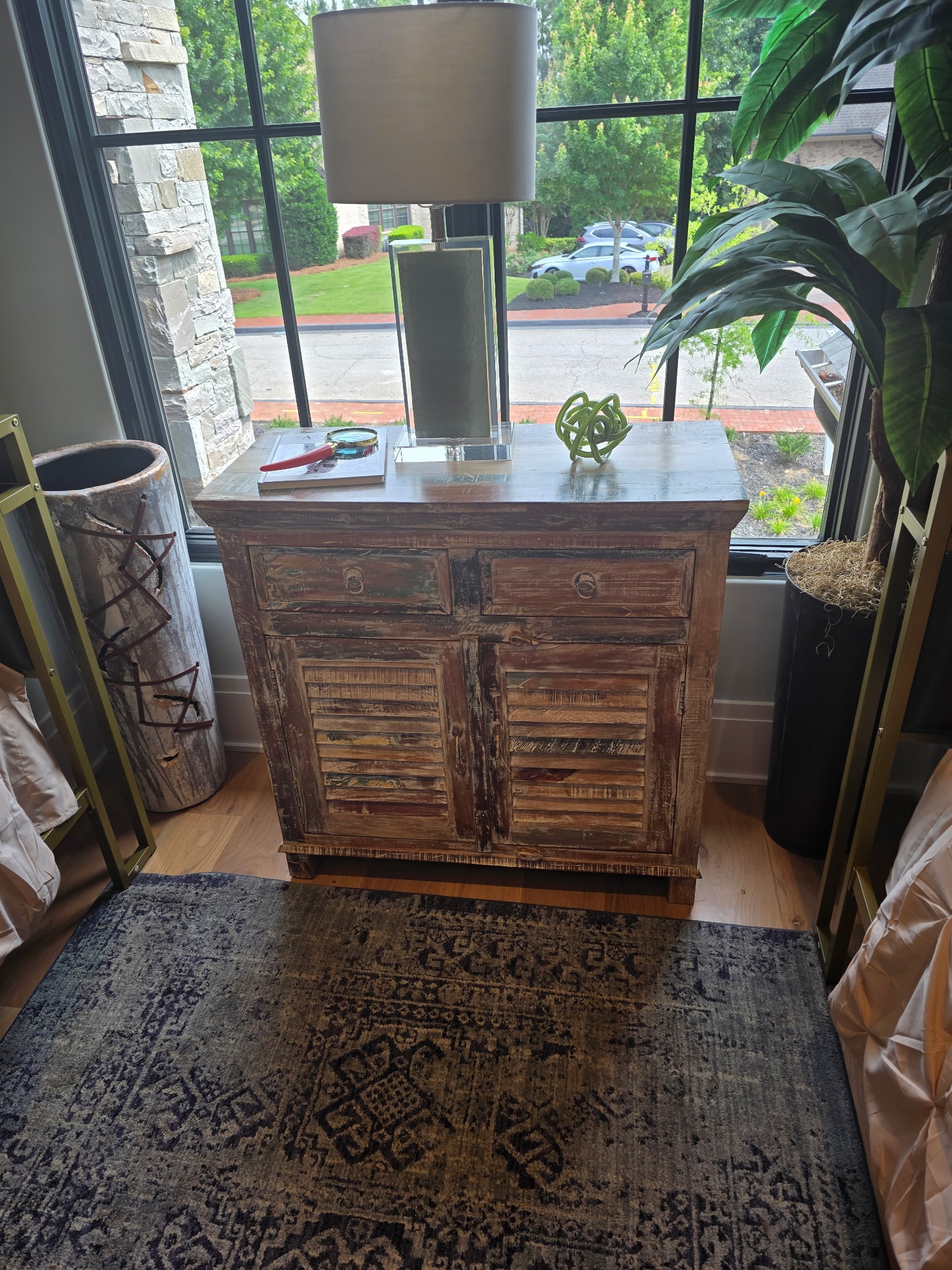 Distressed wood cabinet with shutter doors, lamp, and rug